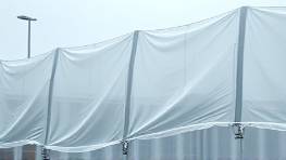 weather-resistant polycarbonate material, frosted texture, testing, photorealistic, outdoor testing facility in harsh weather, highly detailed, wind affecting tarps, 9k resolution, translucent, overcast lighting, shot with a telephoto lens.